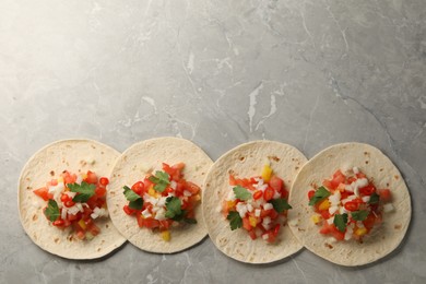 Delicious tacos with vegetables and parsley on grey marble table, top view. Space for text