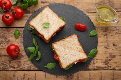 Photo of Delicious Caprese sandwiches with mozzarella, tomatoes, basil and pesto sauce on wooden table, flat lay