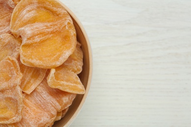 Photo of Delicious dried jackfruit slices in bowl on white wooden table, top view. Space for text