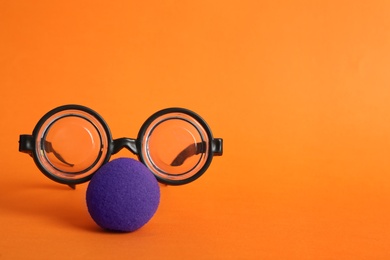Glasses and clown nose on orange background, space for text