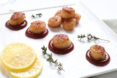 Delicious fried scallops with tomato sauce and lemon on table, closeup