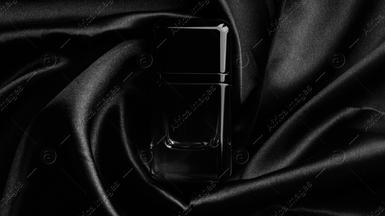 Photo of Luxury bottle of perfume on black silk, top view