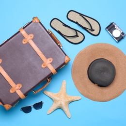Photo of Vintage suitcase and beach objects on blue background, flat lay