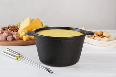 Photo of Fondue with tasty melted cheese, forks and different products on white wooden table