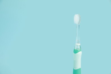 Electric toothbrush on light blue background, space for text