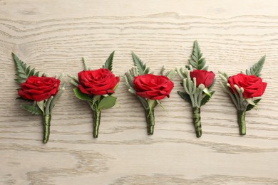 Photo of Many stylish red boutonnieres on light wooden table, flat lay