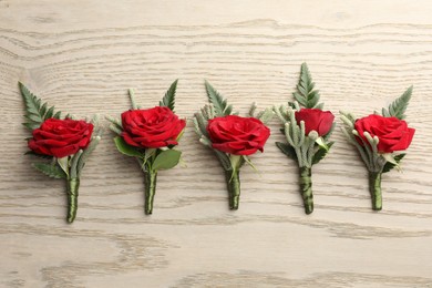 Many stylish red boutonnieres on light wooden table, flat lay