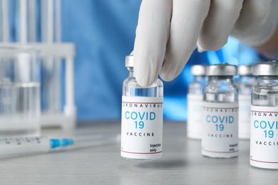 Doctor taking glass vial with COVID-19 vaccine from  table, closeup