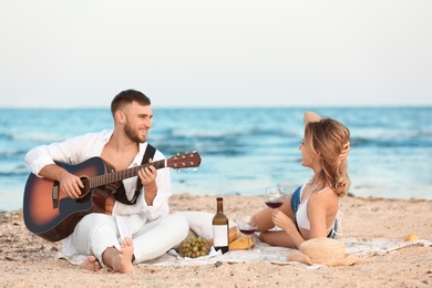 Young couple with guitar having romantic dinner on beach