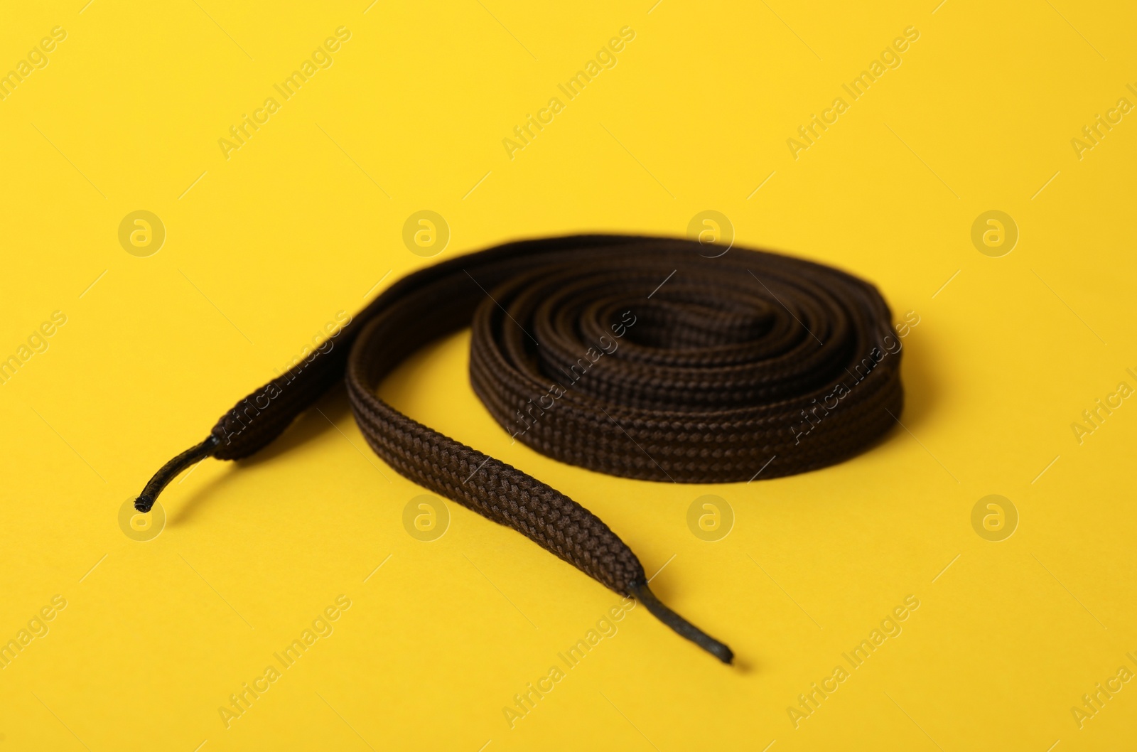 Photo of Rolled dark brown shoe lace on yellow background