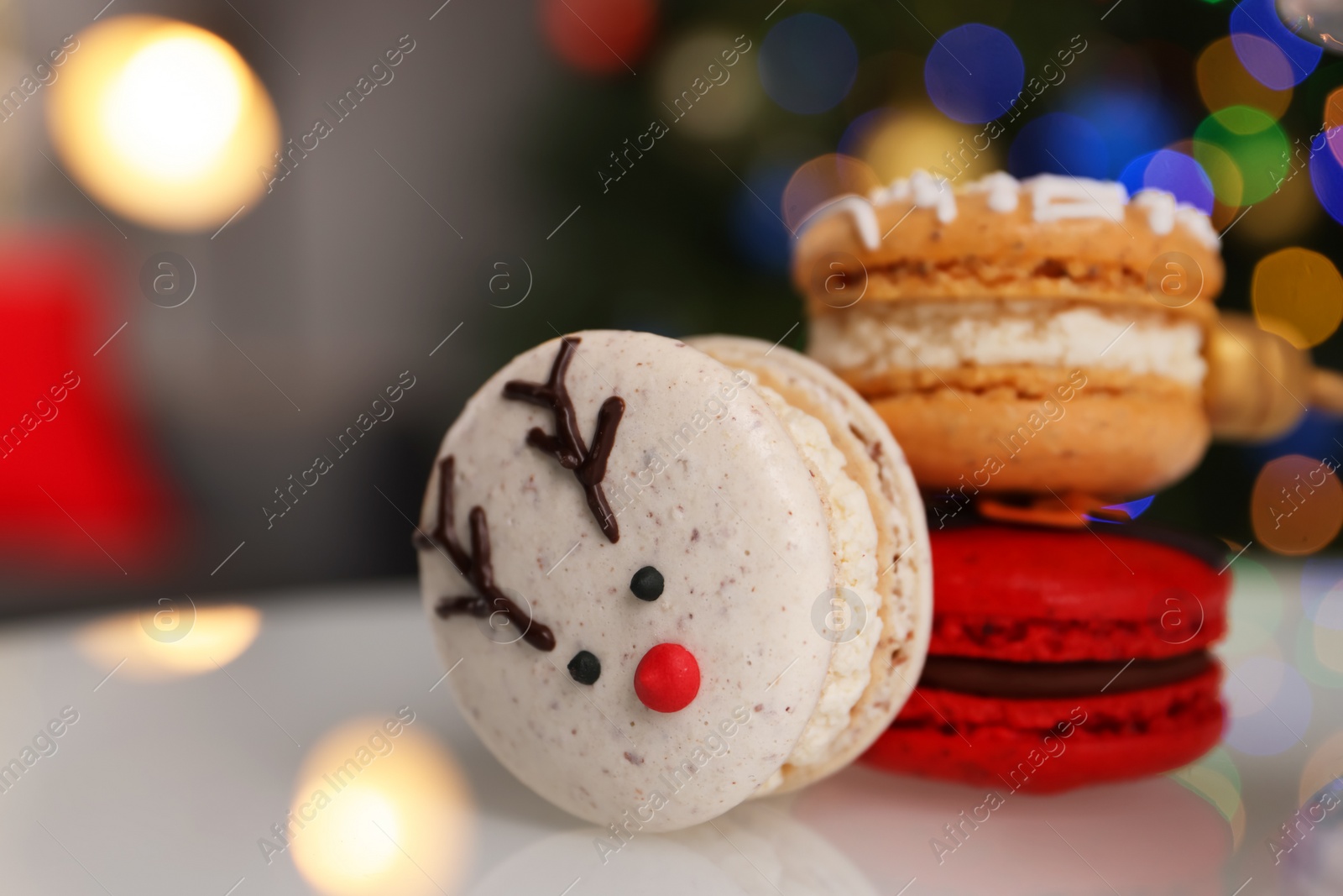 Photo of Beautifully decorated Christmas macarons on white stand against blurred festive lights, closeup