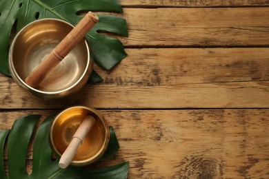 Photo of Golden singing bowls, mallets and monstera leaves on wooden table, flat lay. Space for text