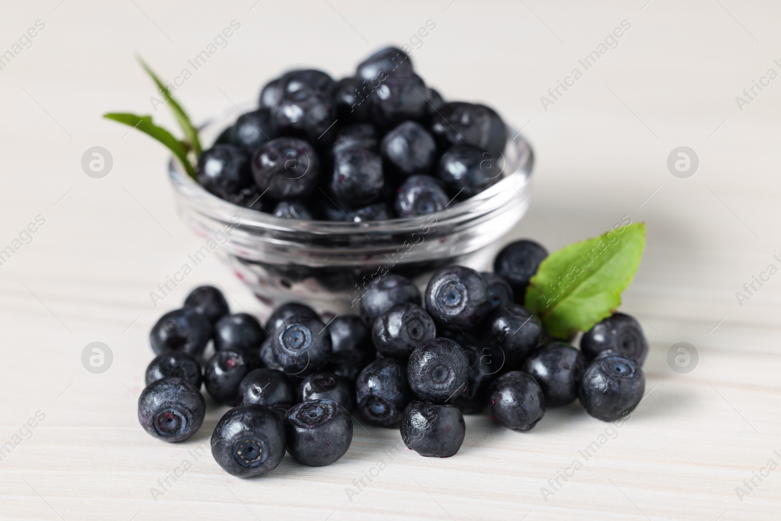 Photo of Ripe bilberries and leaves on white wooden table, closeup