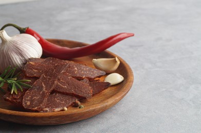 Plate with pieces of delicious beef jerky and spices on light grey table. Space for text