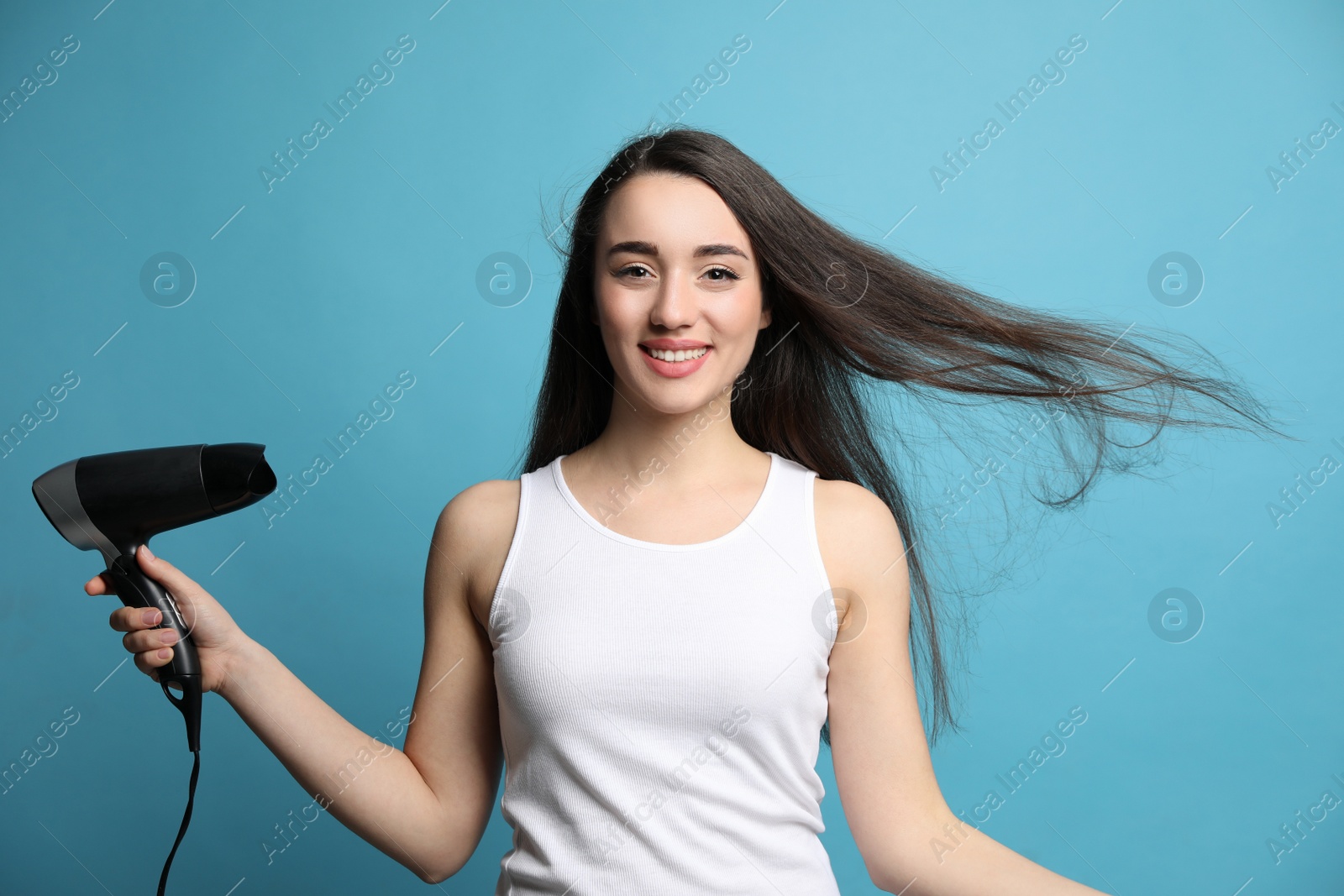 Photo of Beautiful young woman using hair dryer on light blue background