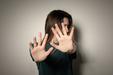 Photo of Young woman making stop gesture against light background, focus on hand