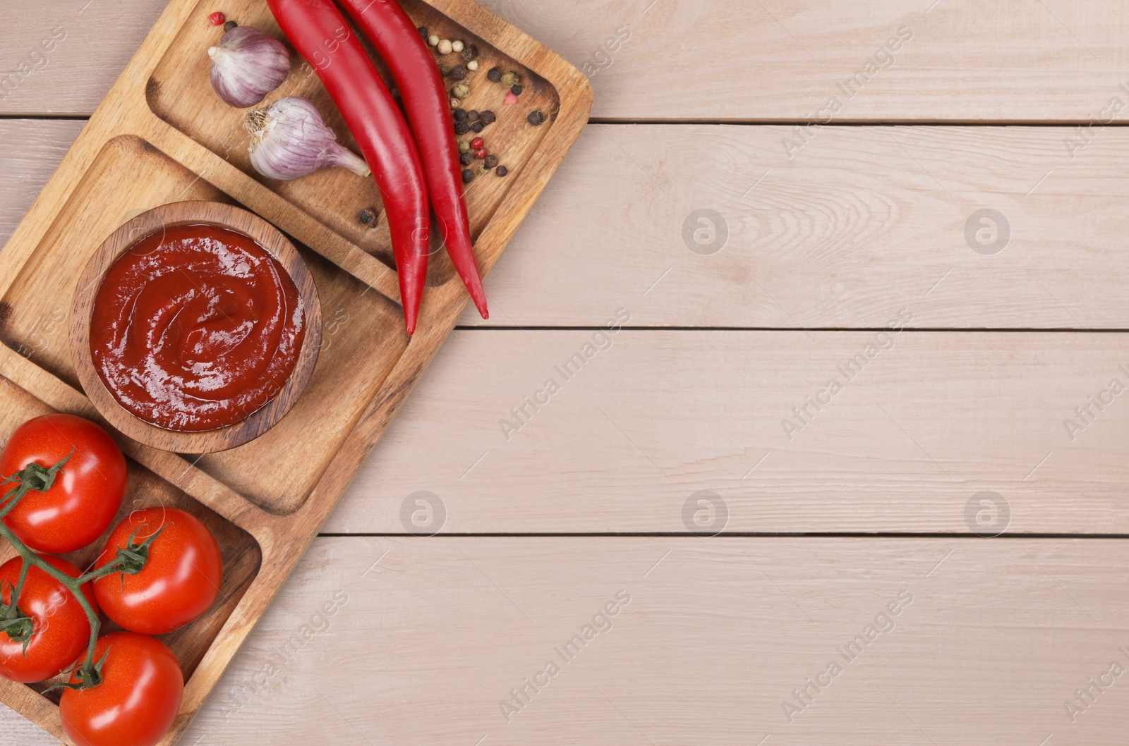 Photo of Plate with delicious ketchup in bowl, peppercorns and products on light wooden table, top view with space for text. Tomato sauce