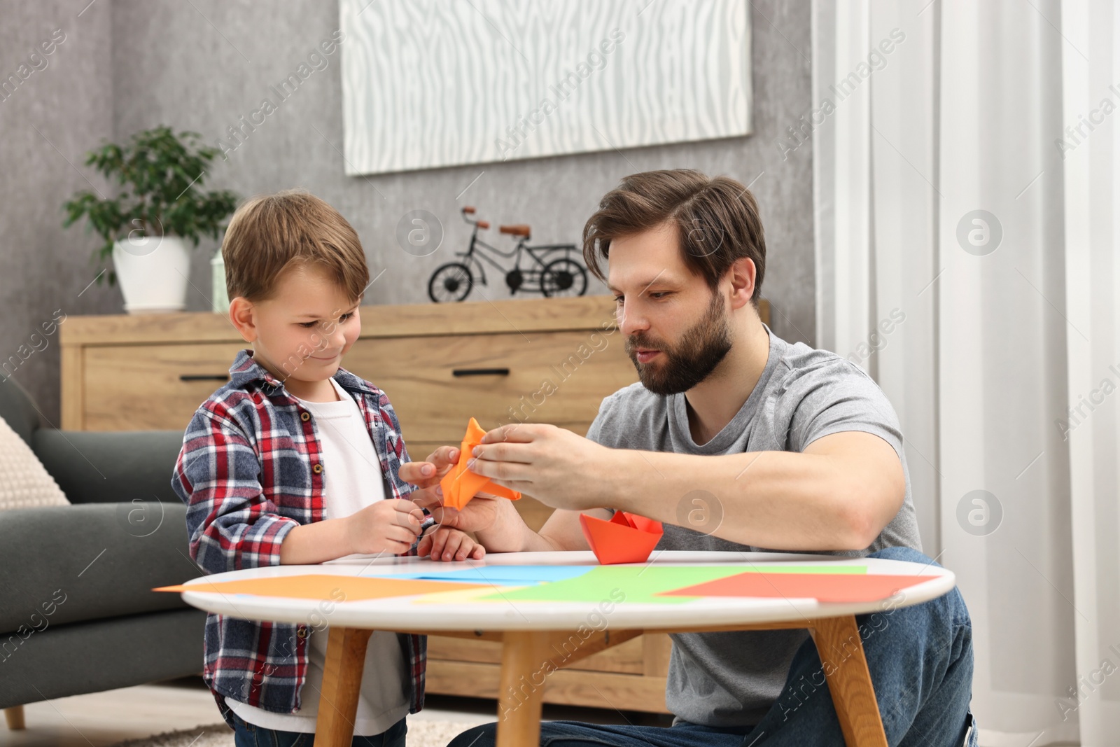 Photo of Dad and son making paper boats at coffee table indoors