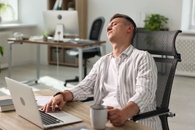 Photo of Man with cup of drink snoozing at wooden table in office