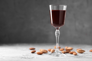 Liqueur glass with tasty amaretto and almonds on light grey table, closeup. Space for text