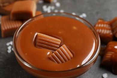 Photo of Tasty salted caramel with candies in glass bowl on grey table, closeup