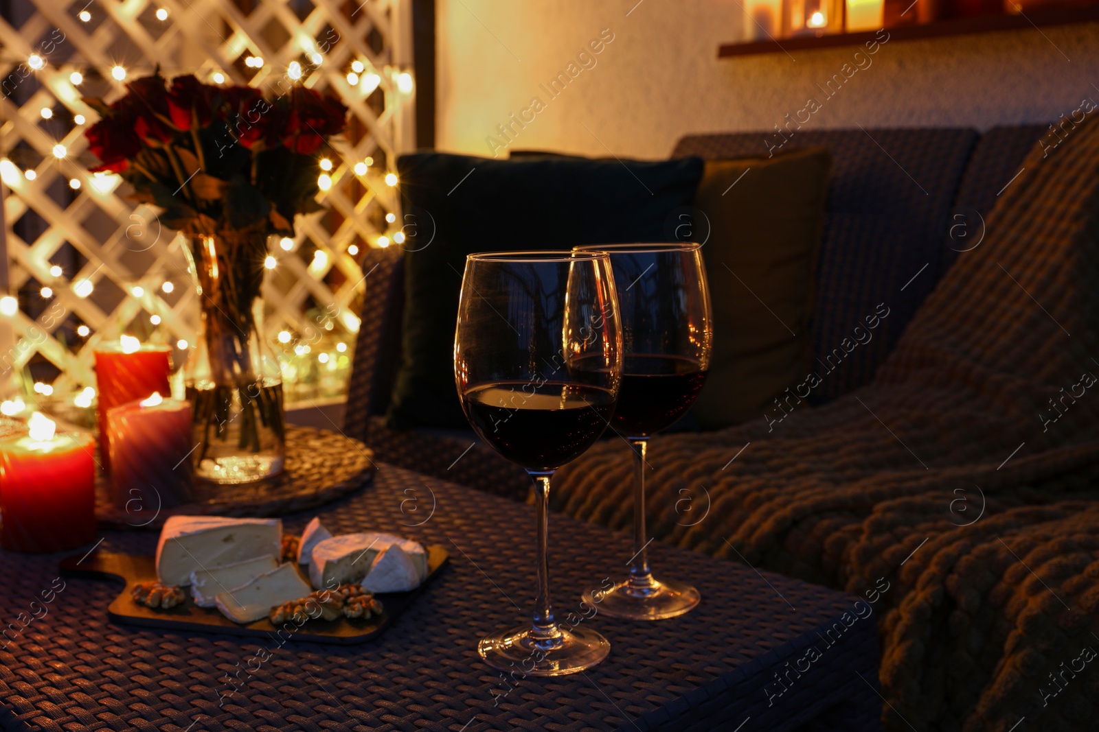 Photo of Glasses of wine, vase with roses, burning candles and snacks on outdoor terrace in evening