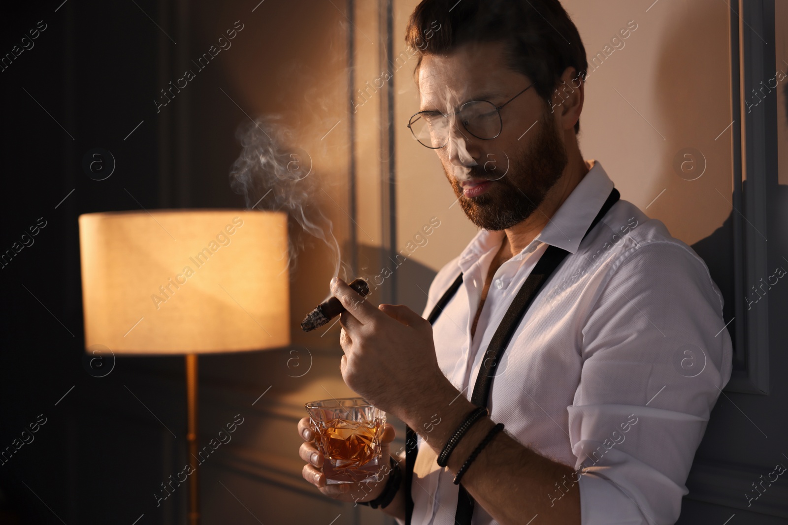 Photo of Handsome man with glass of whiskey smoking cigar at home. Space for text