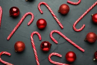 Photo of Tasty candy canes and Christmas balls on black table, flat lay