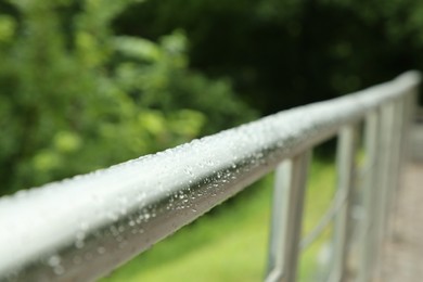 Metal handrail with water drops outdoors, closeup. Rainy weather