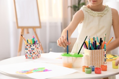 Photo of Little girl painting picture at table indoors, closeup view. Space for text