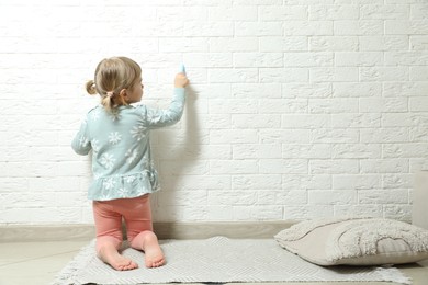 Photo of Little girl drawing on white brick wall indoors, back view and space for text. Child`s art