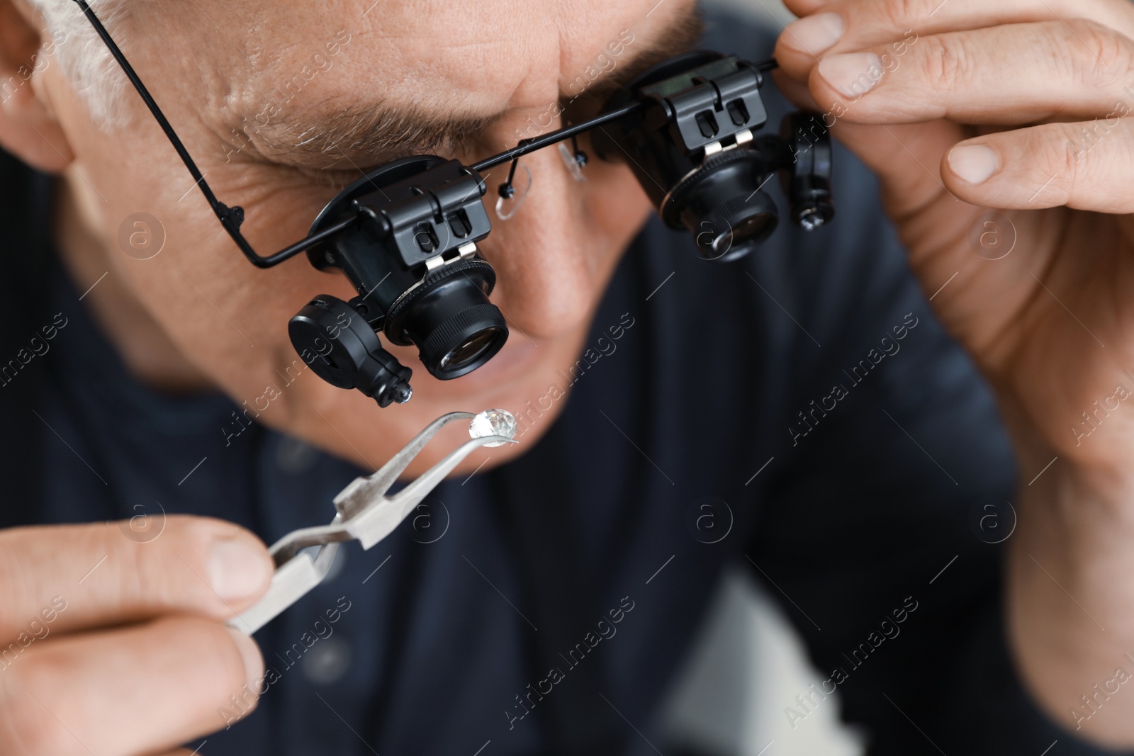 Photo of Male jeweler evaluating precious gemstone in workshop, closeup