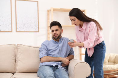 Photo of Young couple arguing about smartphone at home. Problems in relationship