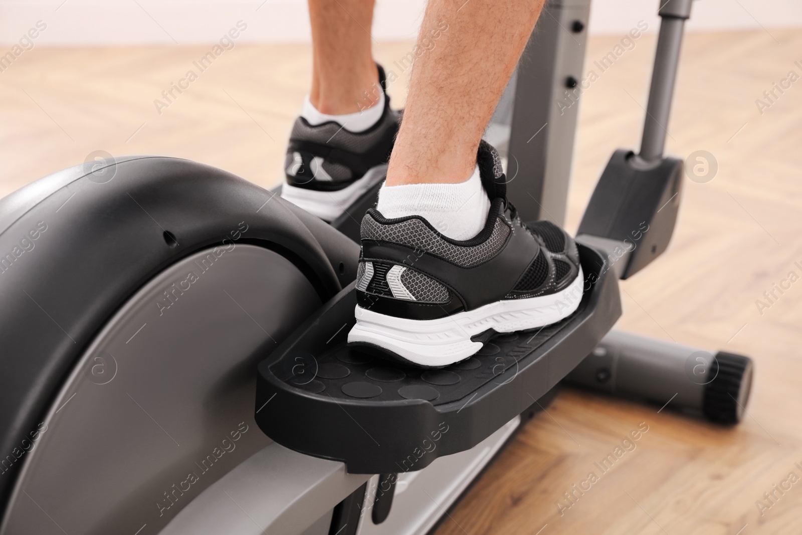 Photo of Man using modern elliptical machine indoors, closeup