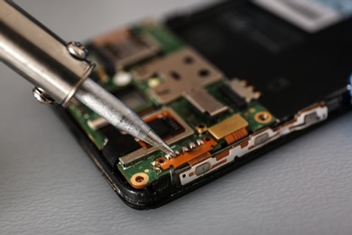 Photo of Repairing broken smartphone with soldering iron on table, closeup. Space for text