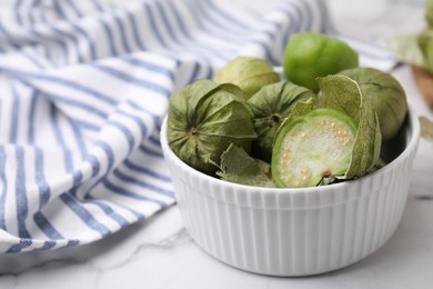 Photo of Fresh green tomatillos with husk in bowl on light table, closeup