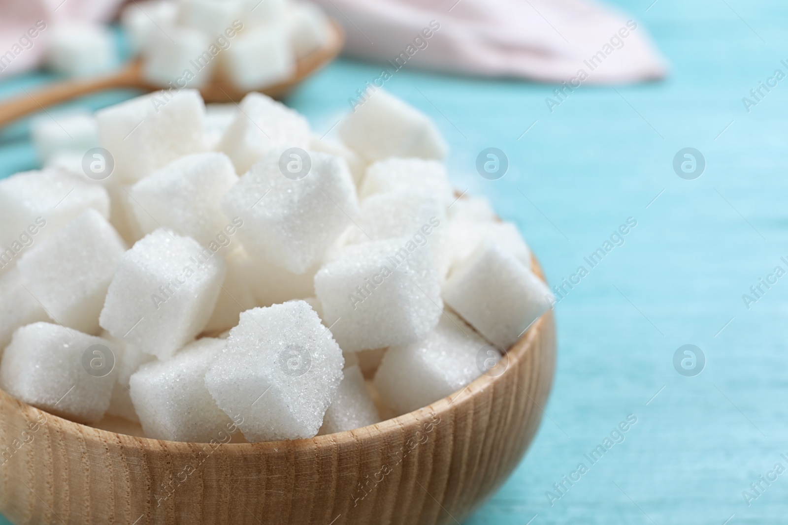 Photo of Refined sugar cubes in bowl on blue wooden table, closeup