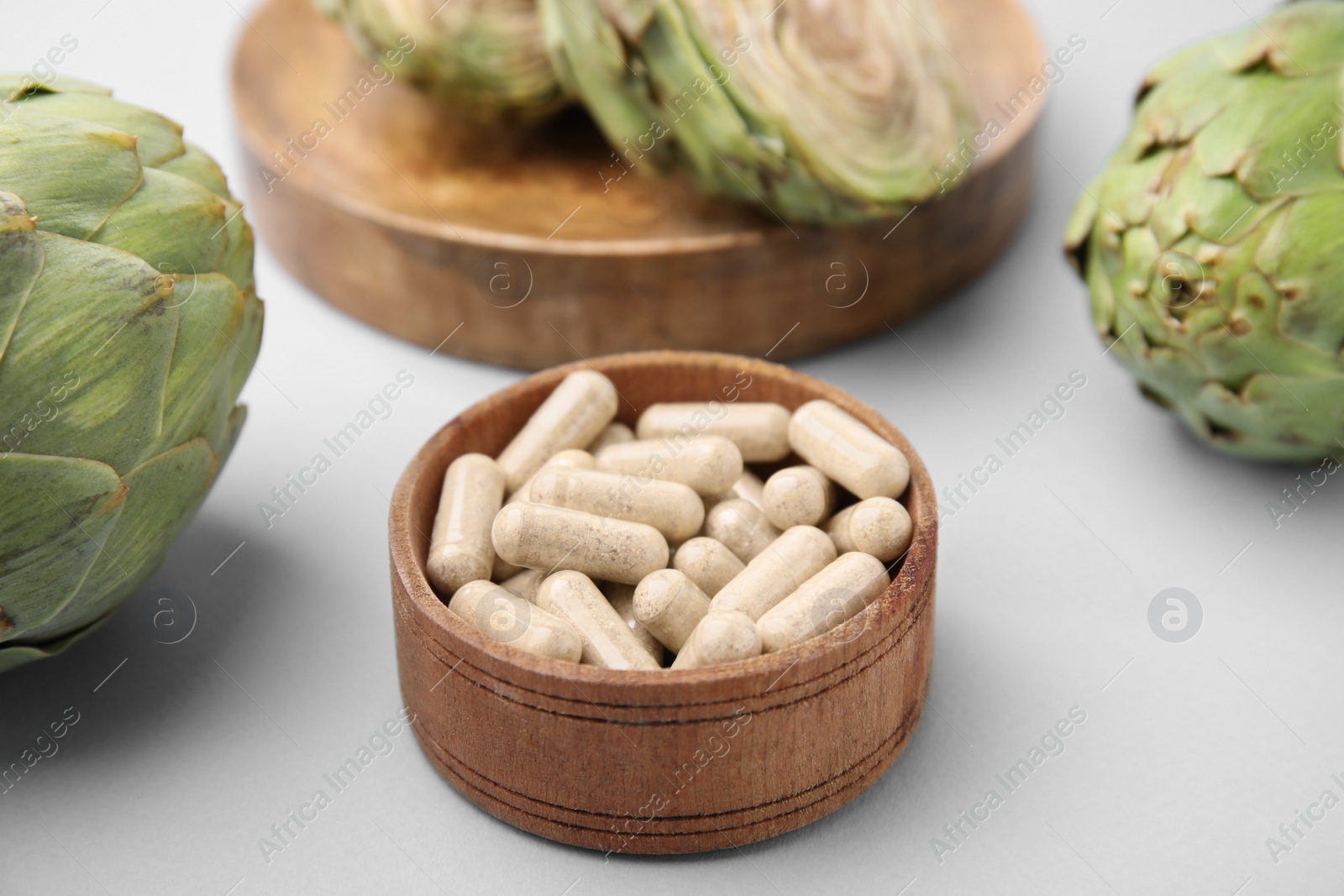 Photo of Bowl with pills and fresh artichokes on light grey background, closeup