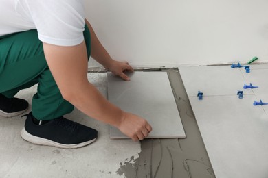 Photo of Worker installing ceramic tile on floor, closeup