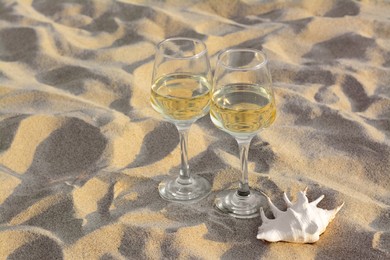 Photo of Glassestasty wine and seashell on sand, space for text