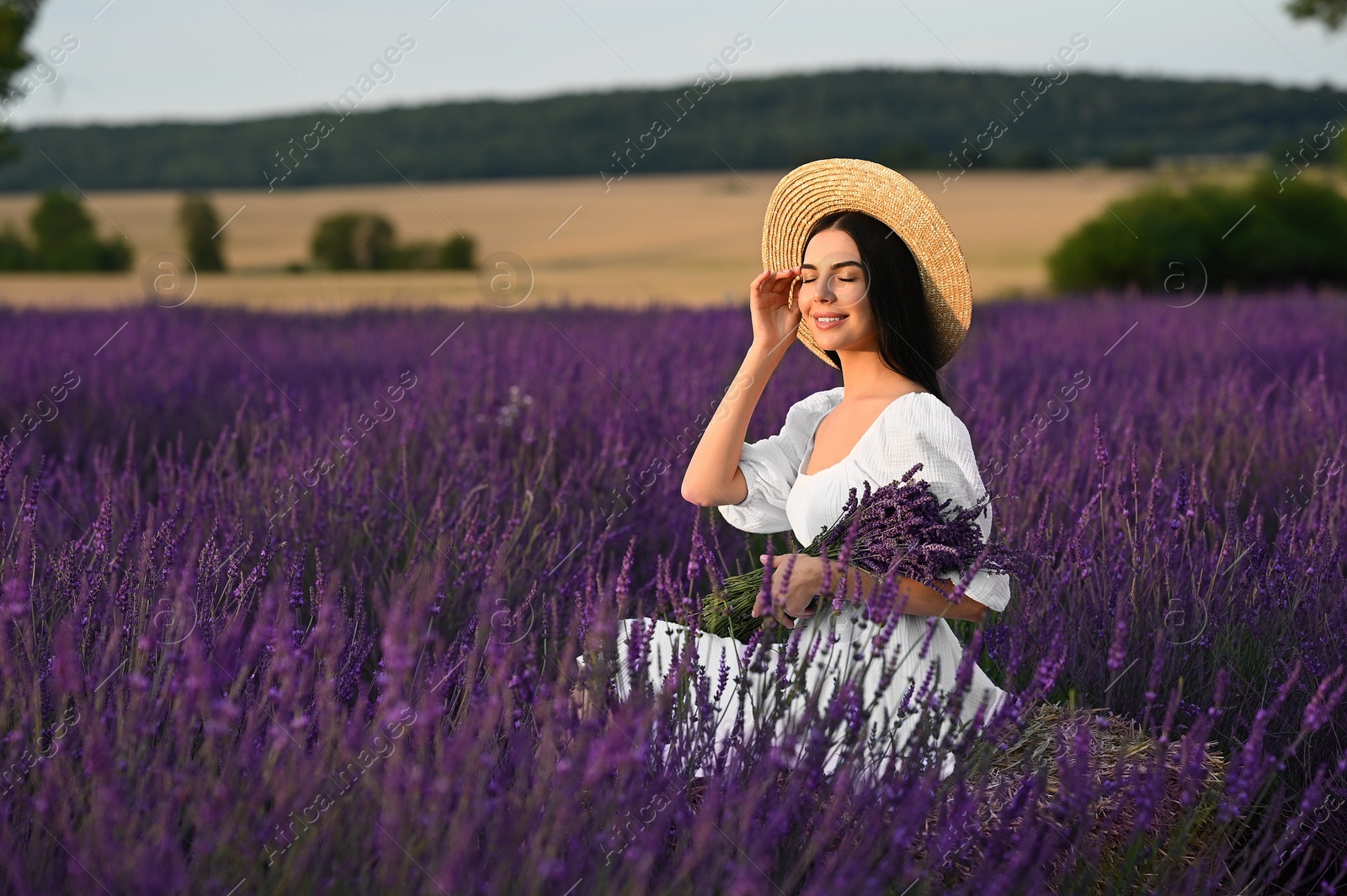 Photo of Beautiful young woman with bouquet sitting in lavender field