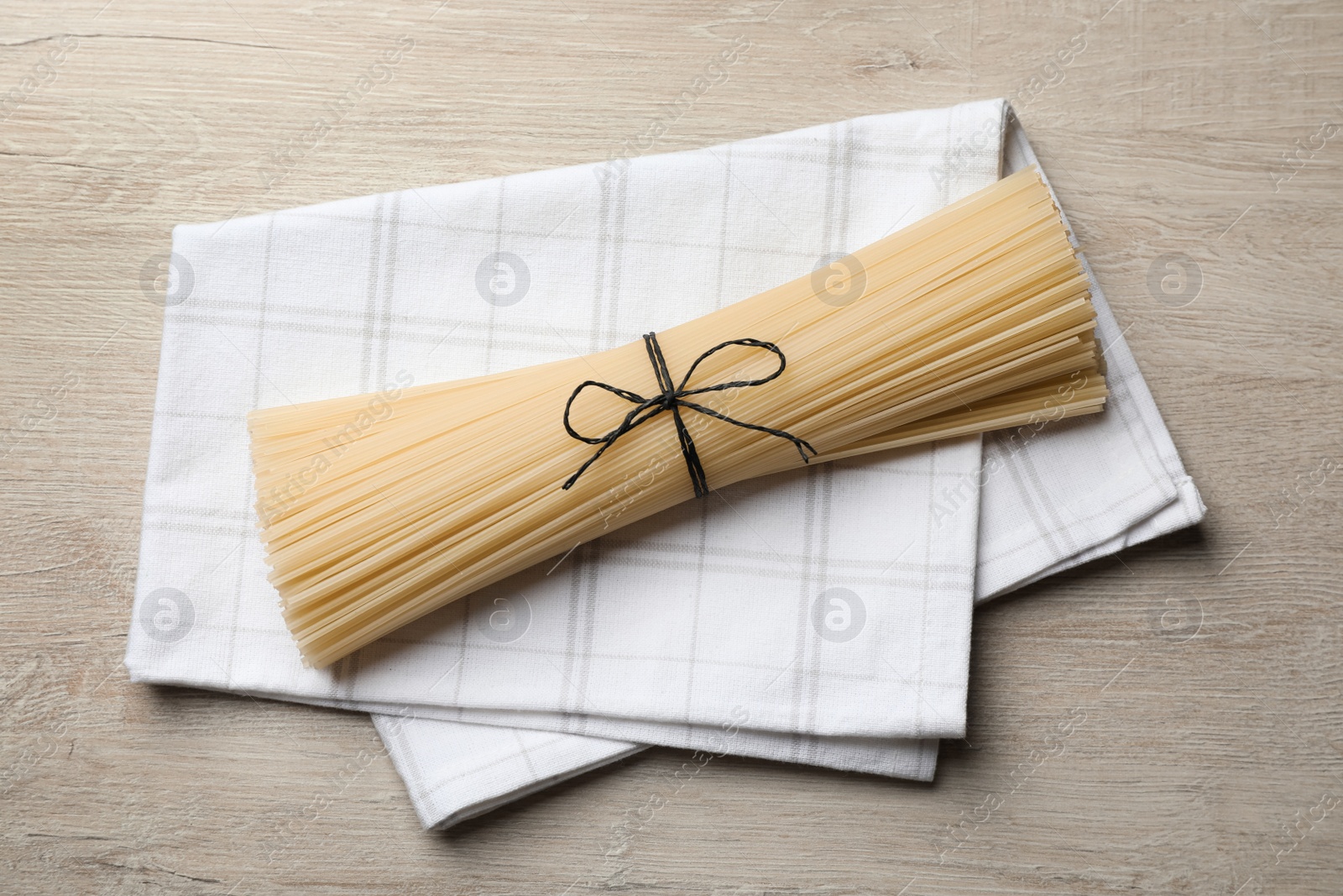 Photo of Uncooked rice noodles with napkin on wooden table, top view