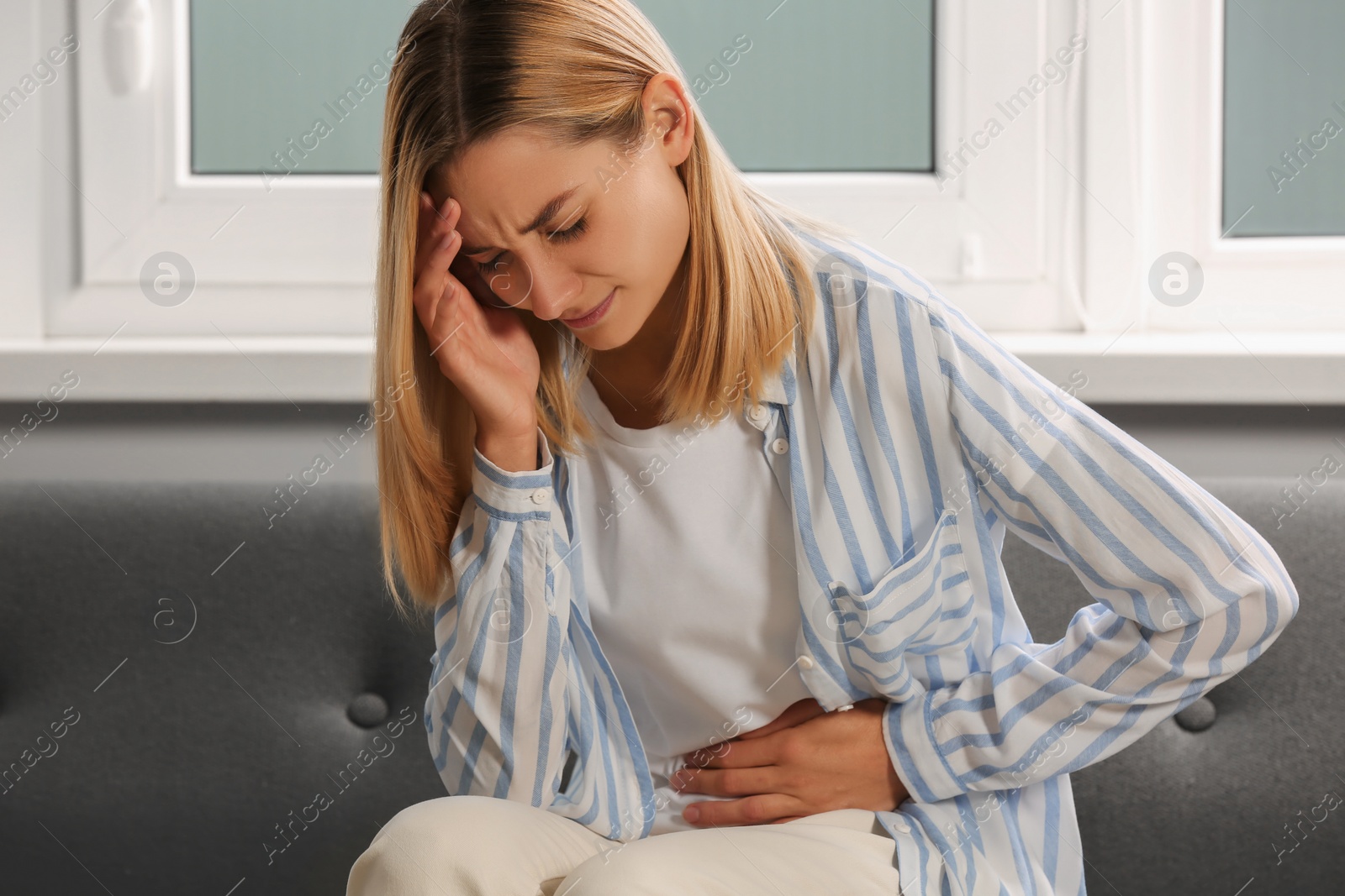 Photo of Young woman suffering from menstrual pain on sofa indoors