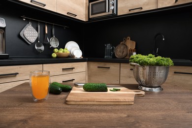 Cucumbers, lettuce and glass of juice on wooden table in kitchen