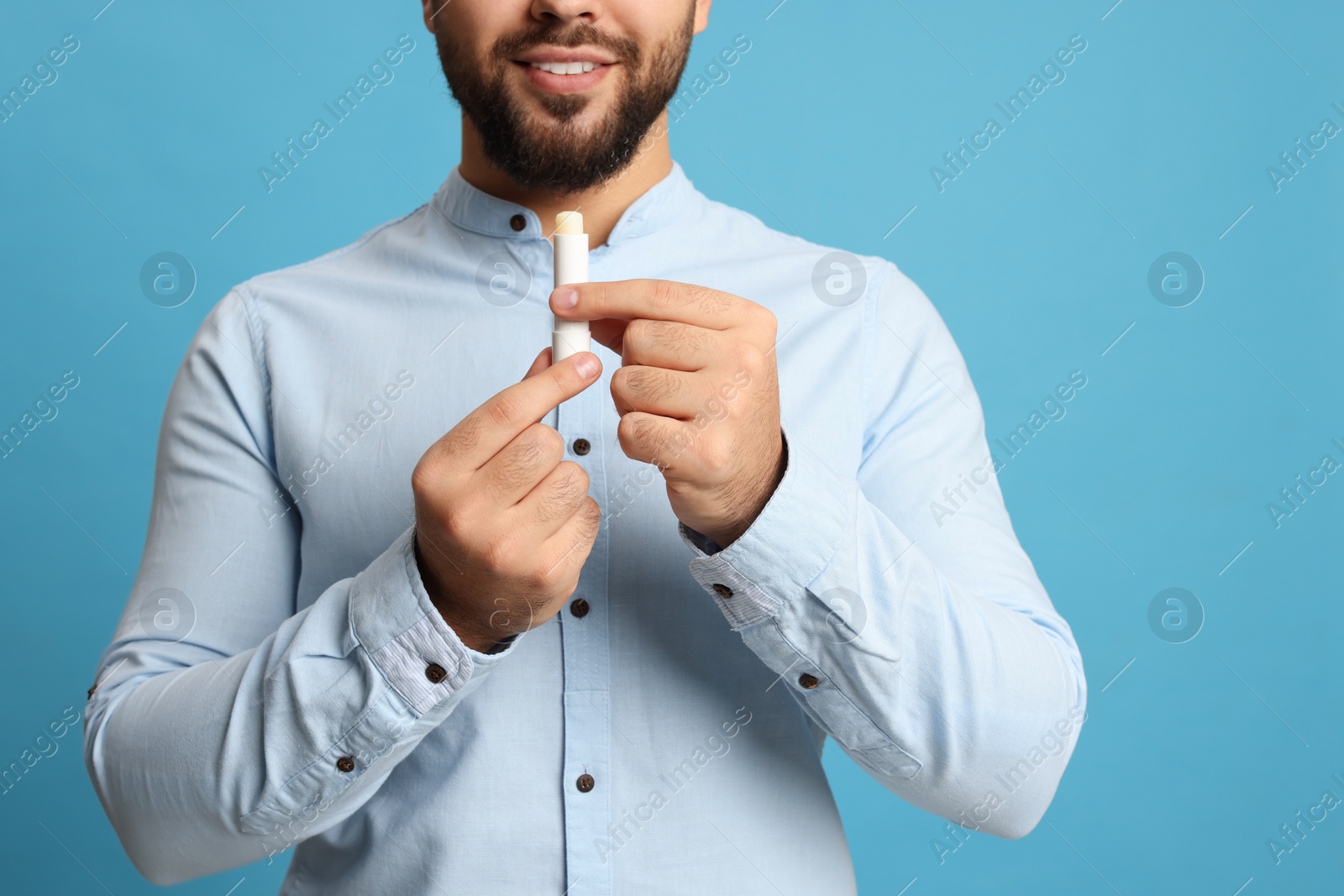 Photo of Young man with lip balm on turquoise background, closeup