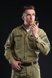 Male security guard using portable radio transmitter on dark background