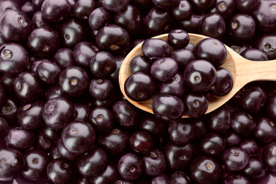 Wooden spoon and fresh ripe acai berries as background, closeup