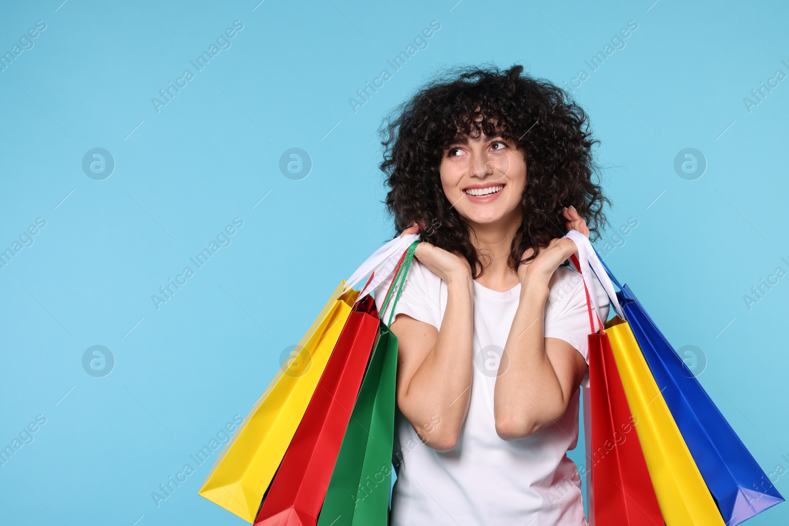 Photo of Happy young woman with shopping bags on light blue background