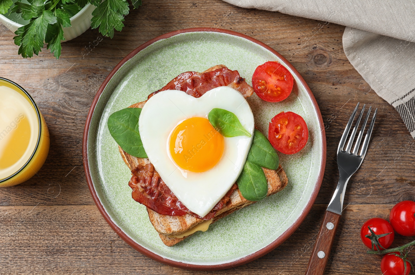 Photo of Tasty sandwich with heart shaped fried egg and bacon on wooden table, flat lay