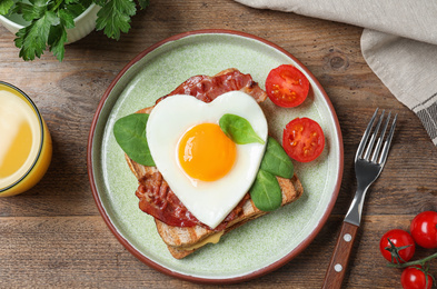 Tasty sandwich with heart shaped fried egg and bacon on wooden table, flat lay